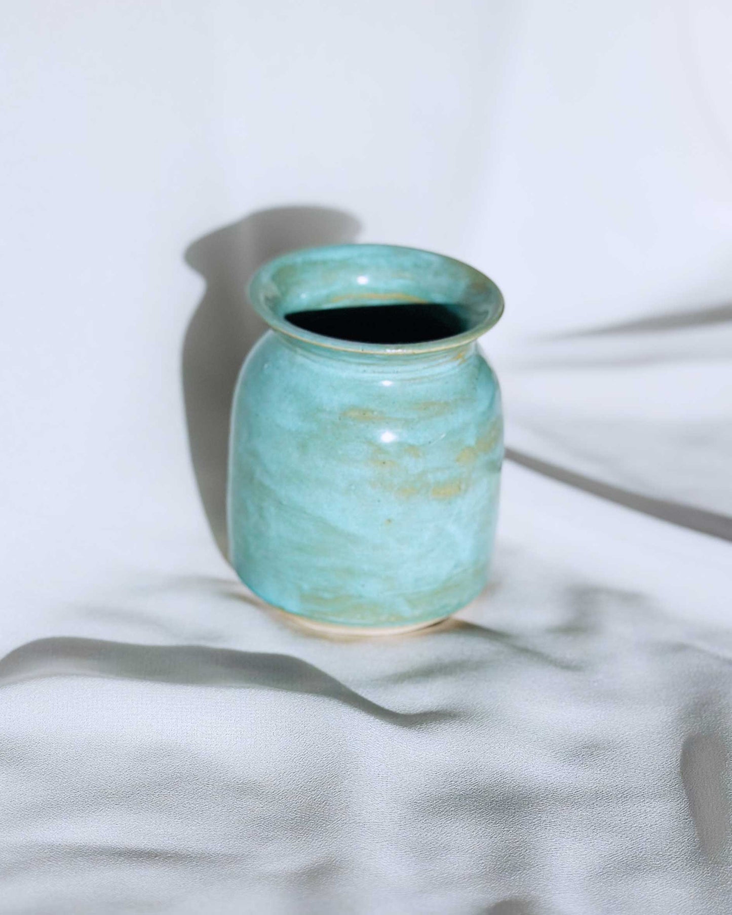 Turquoise ceramic vase on a white fabric background