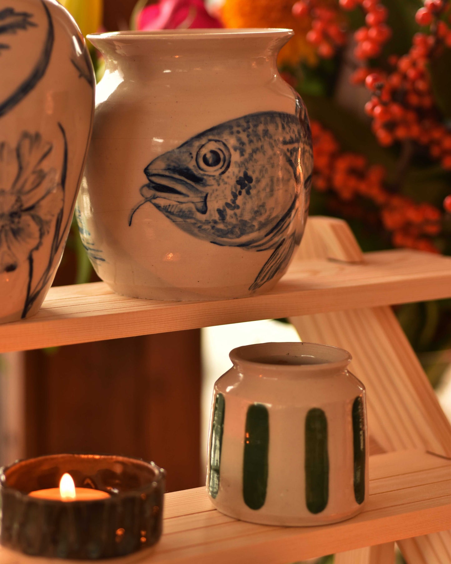 Ceramic jars with fish design on a wooden shelf with a lit candle.