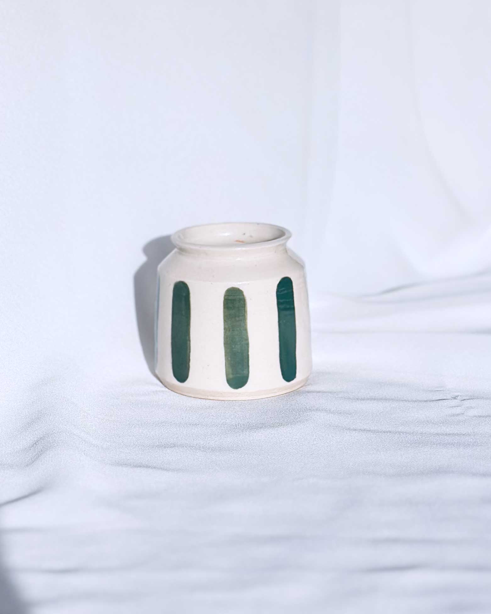 White ceramic jar with green vertical stripes on a light blue background