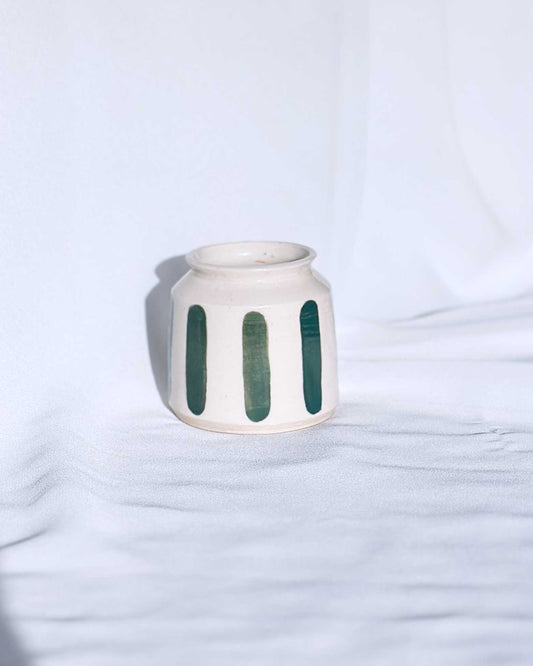 White ceramic jar with green vertical stripes on a light blue background