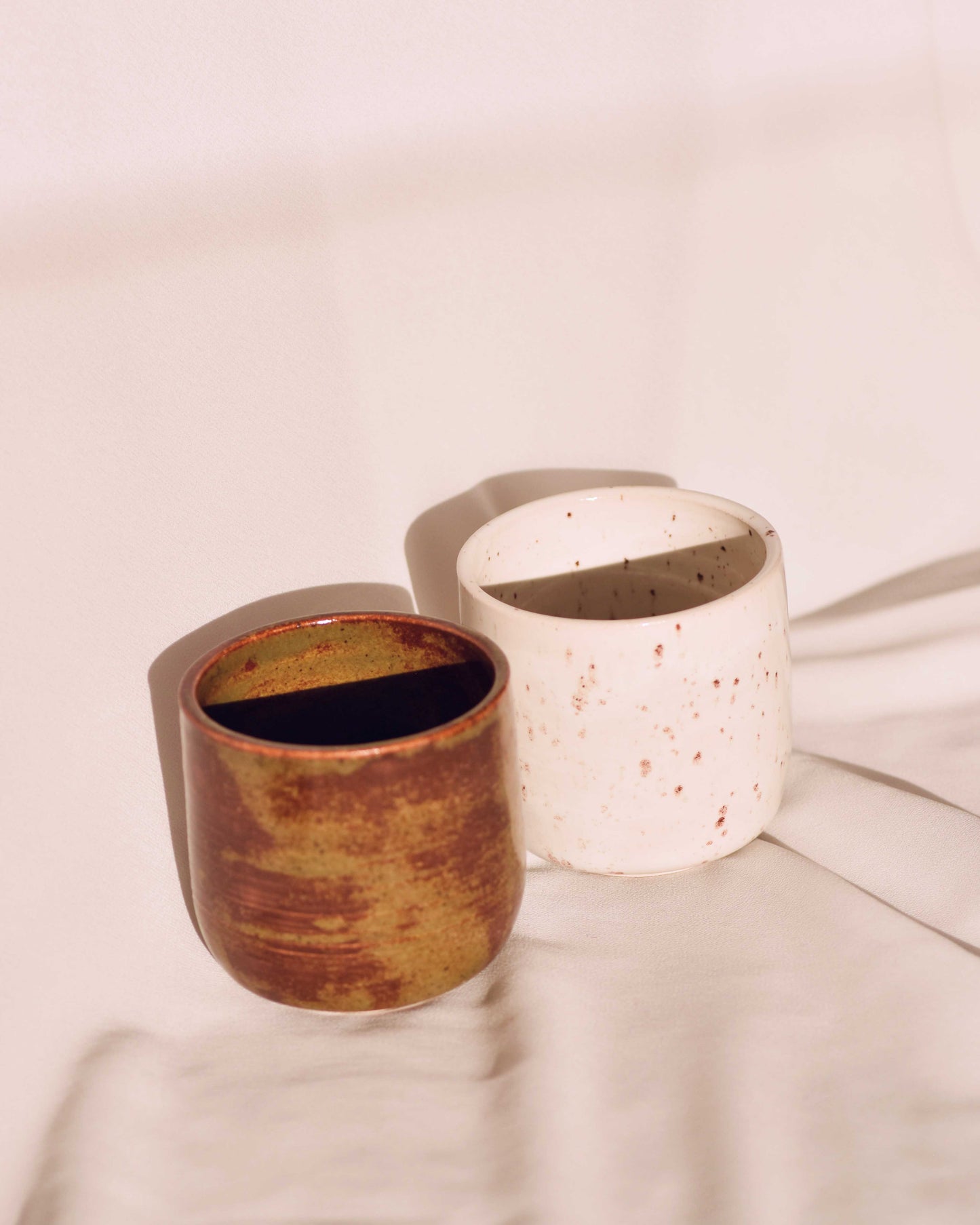 Two ceramic pots, one brown and one white with speckles, on a light surface.