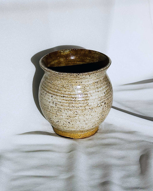 Ceramic vase with speckled glaze on a textured white surface