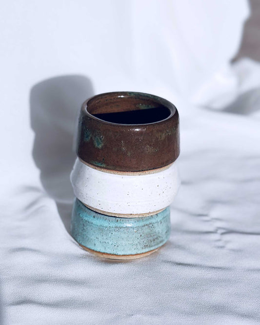 Stack of ceramic cups with brown, white, and blue glaze on a light fabric background
