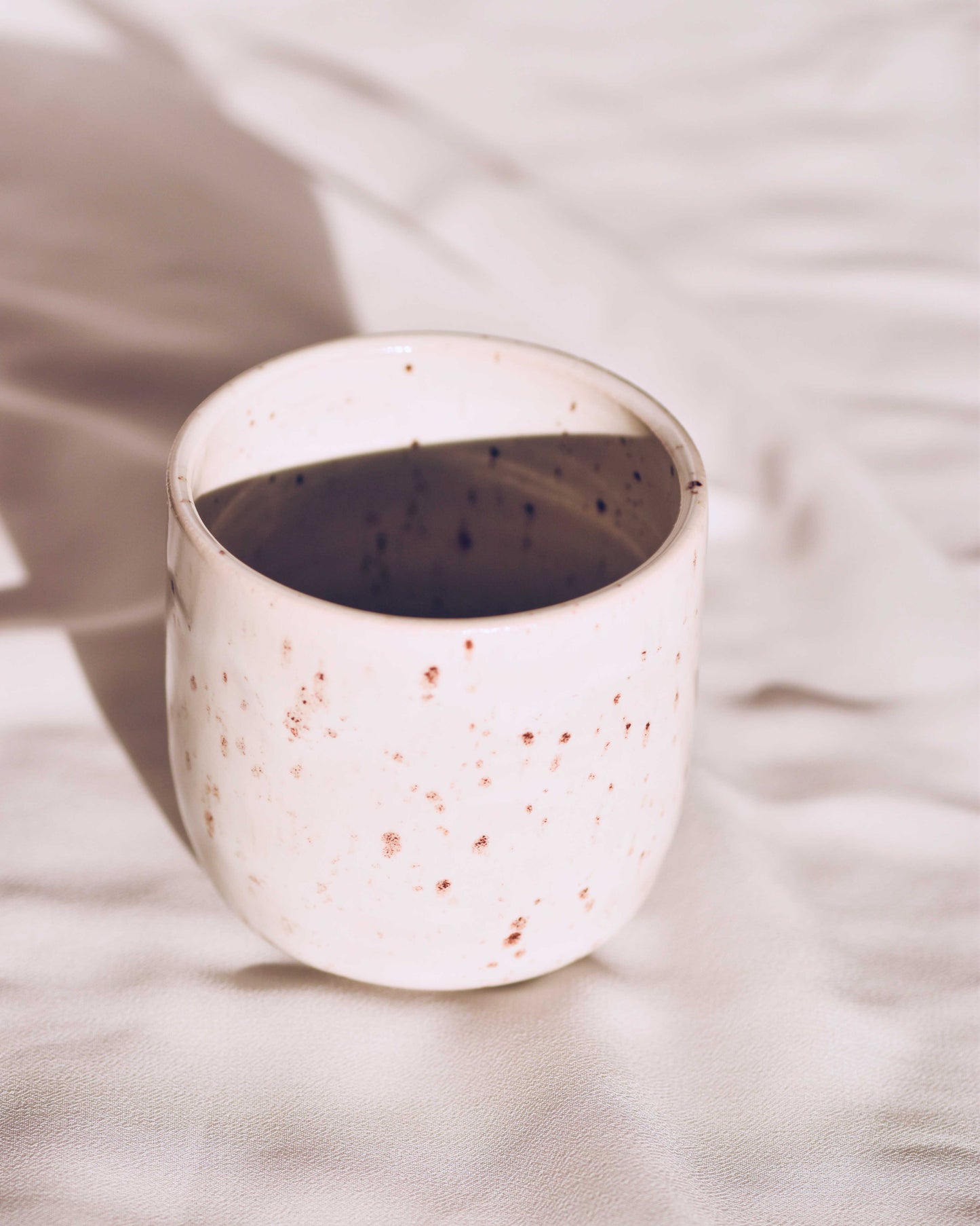 White ceramic cup with speckled pattern on a light fabric background
