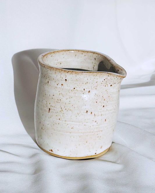 White ceramic pitcher with brown speckles on a white background